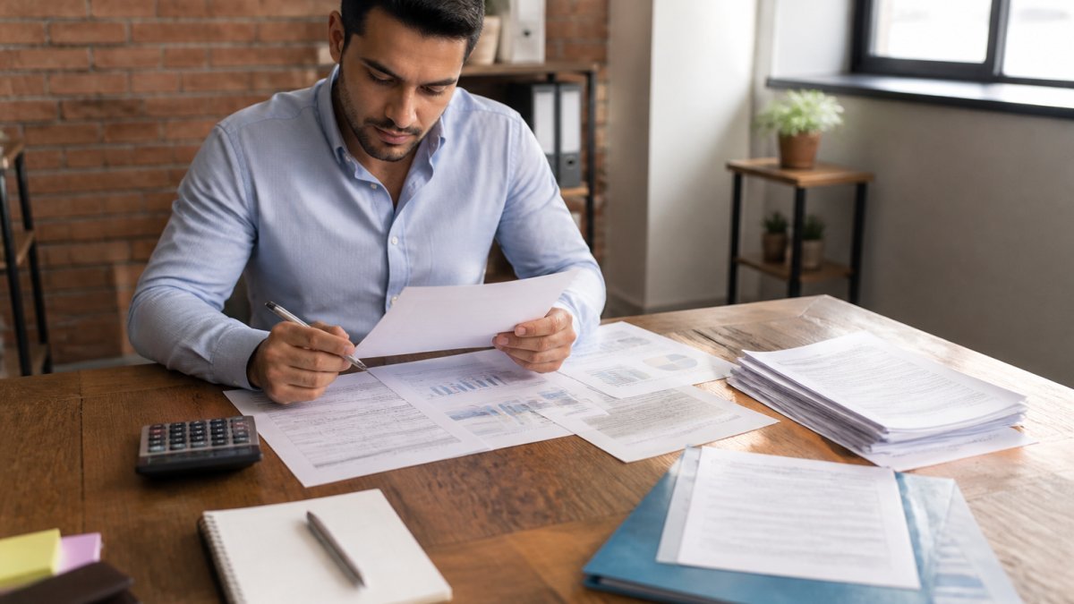Professional reviewing financial documents and credit reports at desk with calculator and notebook, focused on planning mortgage preparation with organized papers and charts